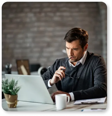 A man sitting at a desk looking at his laptop, working on building his online presence and optimizing SEO keywords with the help of ProntoWriters, a renowned provider of content writing services.