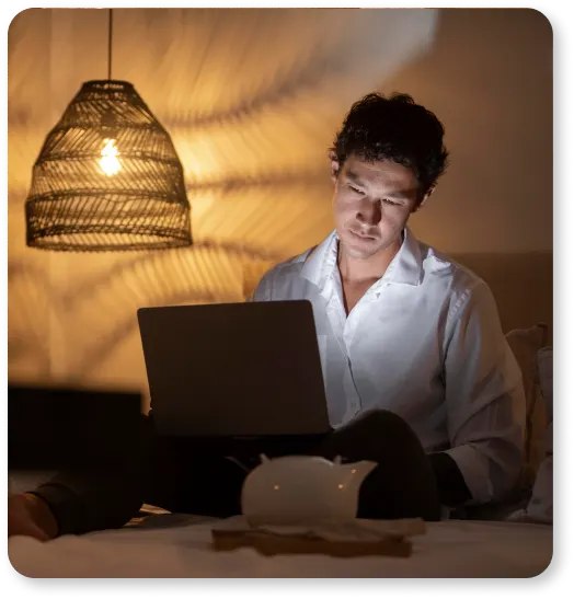 A man using a laptop in bed at night while working for ProntoWriters, one of the professional content writing services.