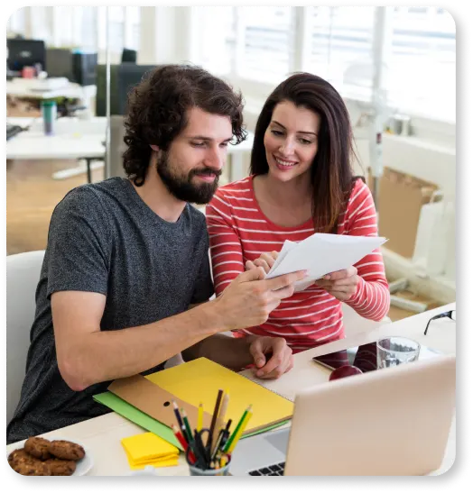 A man and woman, representing an online presence, are seen examining a piece of paper in front of a laptop.